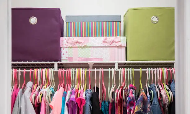 A colorful, organized shared kids’ closet with dual hanging sections, color-coded drawers, and tidy shelves in a bright bedroom.