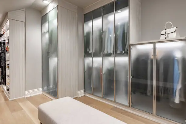 A sleek floor-to-ceiling closet cabinet with backlit glass doors and crown molding, enhancing a tall room’s elegance.