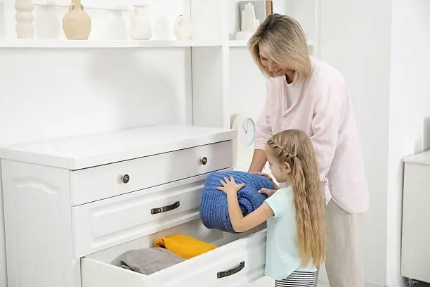 A parent and child organizing a tidy, safe closet with low shelves and secure hardware in a cozy room.
