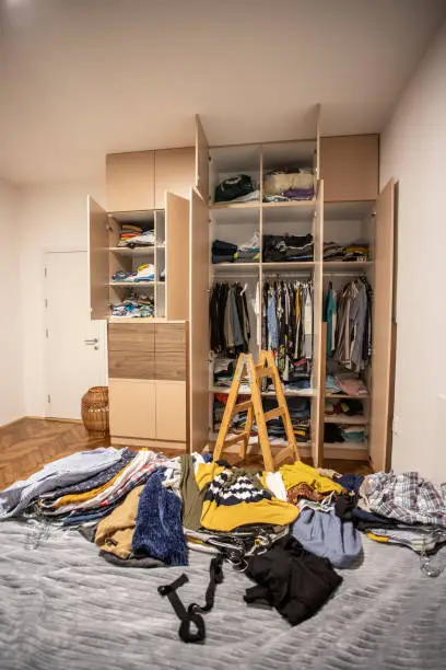 A messy bedroom closet with clothes spilling out, showing the need for a custom reach-in closet to organize the space