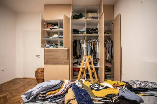 A cluttered bedroom wardrobe with scattered clothes, highlighting the need for organized custom storage