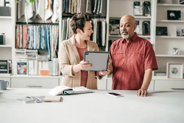 A designer in a showroom discussing home office closet designs with a client, using 3D renderings on a tablet