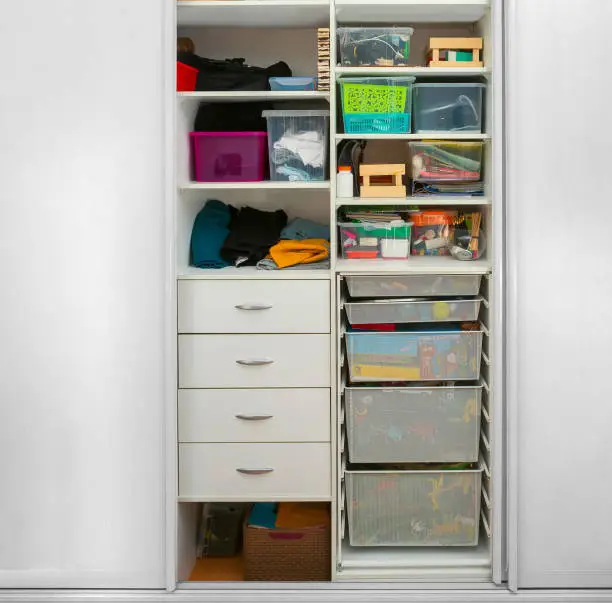 A reach-in closet in a kids’ room with low rods, colorful bins, and compact shelves for toys and clothes