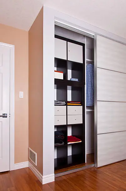A sleek, compact closet in a small bedroom with sliding doors, vertical shelves, and built-in organizers, showcasing efficient storage