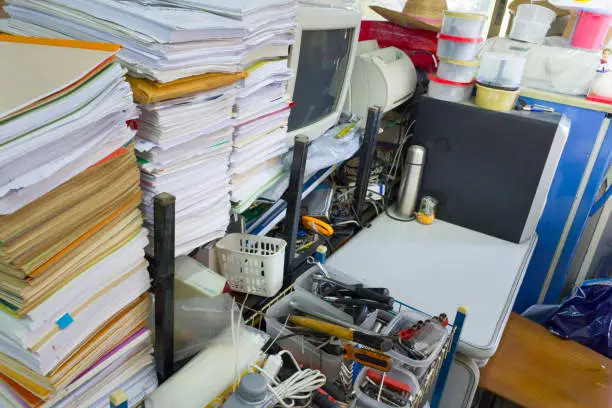 A cluttered home office with scattered papers and cables, showing the need for a custom closet system to organize
